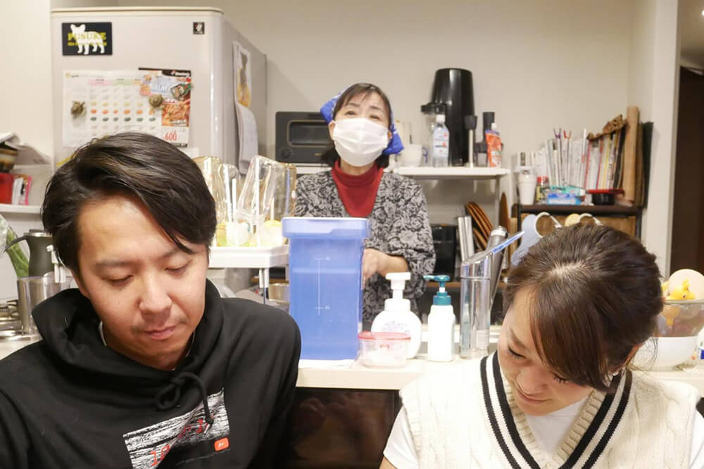 池田ご夫妻の後ろのキッチンに立つ黒田ママ