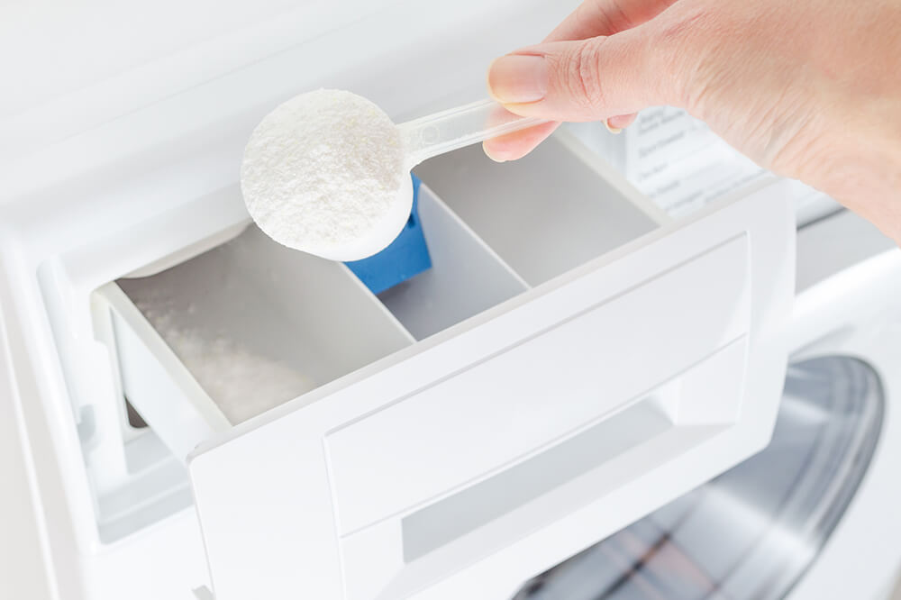 洗剤をスプーンですくって洗濯機に入れるところ